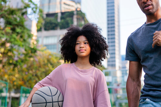 Girl with basketball and man on court in city.
