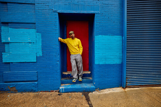 Casual man stands in the doorway of a blue building. 