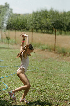 Happy Girl Running and Playing with Water in Sunny Backyard