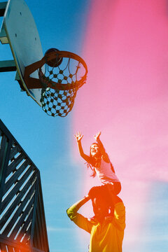 A Child Stands on an Adult's Shoulders at a Basketball Court