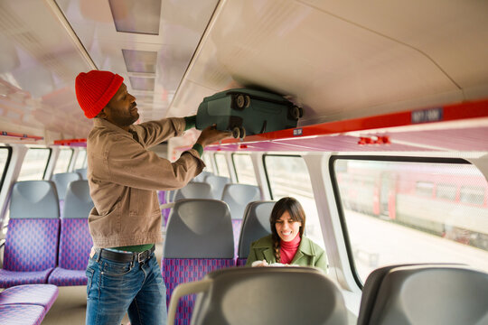 Man Places Suitcase Above Seat in Train While Woman Smiling