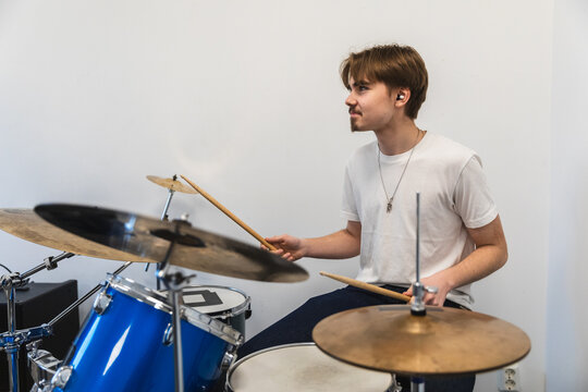 Young man playing a blue drum kit in a bright room