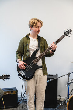 Young man playing a black bass guitar in a rehearsal room