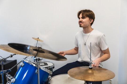 Young man playing a blue drum kit in a bright room