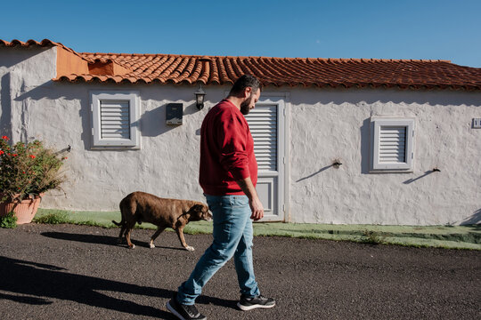 Man walking dog beside white house with tile roof