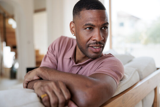 Man in pink shirt rests on sofa, looking away.