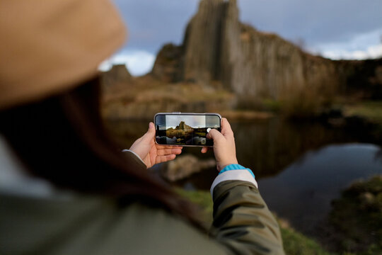 Traveler photographing basalt columns by reflective lake