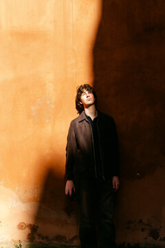 Young man leaning againts a terracotta wall in Lyon France. 