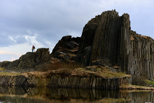 Hiker on basalt columns rock formation by lake