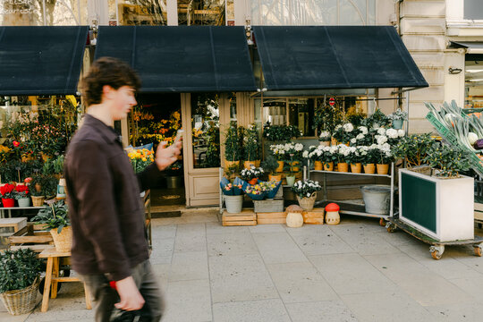 young man looking at phone walking on front of a flower shop in Lyon