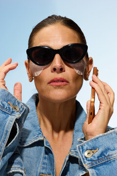 Woman With Sunglasses Uses Phone and Wears Eye Patches Outdoors