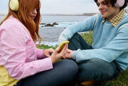 Couple using smartphones while sitting by coast Galicia Spain