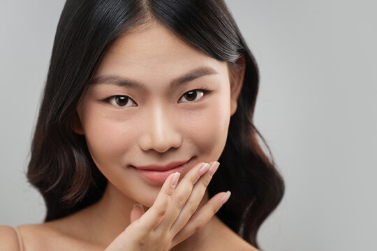 Beautiful Asian woman with flawless skin gently touches her chin