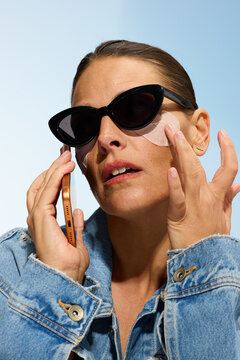 Woman Applying Skincare While Using Her Phone in Daylight