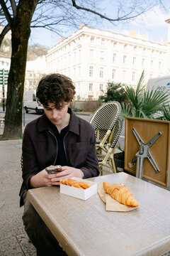 young man sitting in caf&eacute;,  croissant and bugne in Lyon France