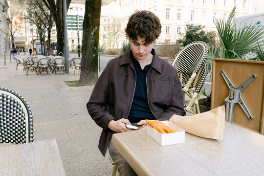 young man sitting in caf&eacute;,  croissant and bugne in Lyon France