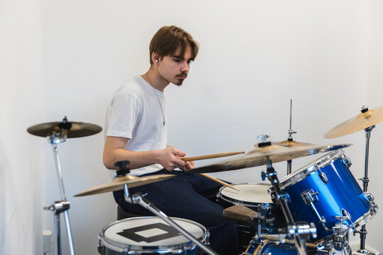 Young man playing a blue drum kit in a bright room