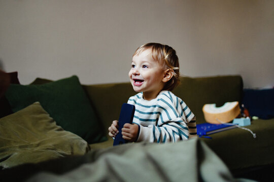Smiling Toddler On Couch Holding Remote In Living Room