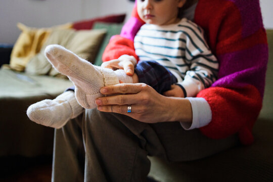 Mother Helping Toddler Put On Socks While Sitting At Home