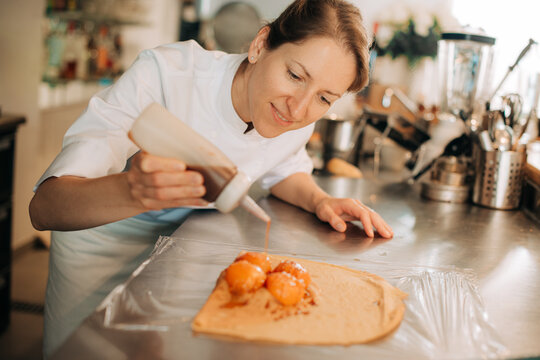 Chef drizzling sauce over apricot crepe dessert