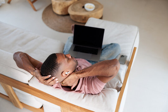 Man relaxing on couch with laptop and earbuds.