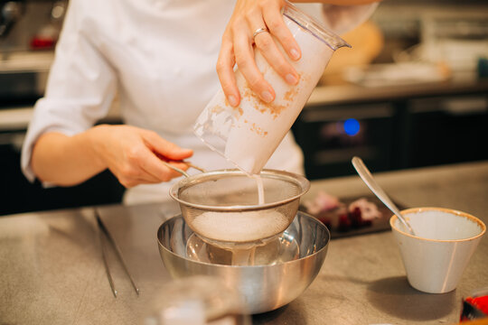 Chef straining sauce through sieve in professional kitchen