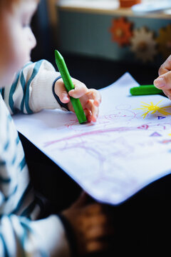 Child Drawing With Green Crayon At Table