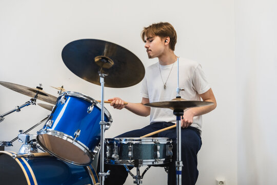 Young man playing a blue drum kit in a bright room