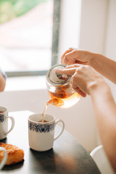 Pouring hot tea into cup in bright kitchen close up