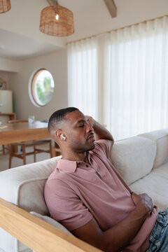 Man relaxing on couch with earbuds in modern home.