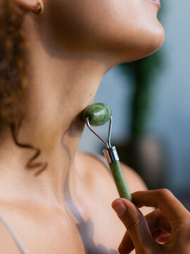 Woman Uses Jade Roller on Her Neck in Indoor Setting