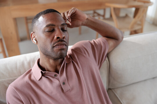 Man relaxing on couch with eyes closed, listening to music.