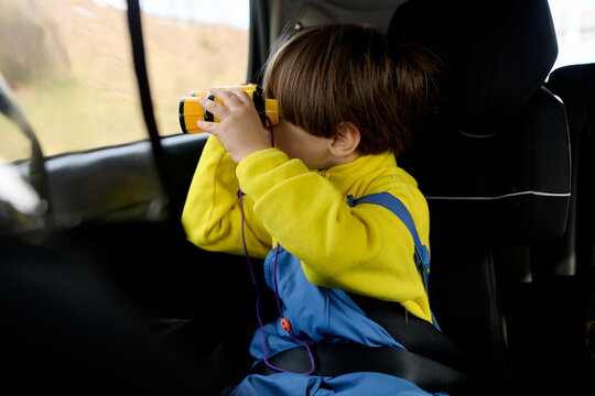 Child looking through binoculars in car seat