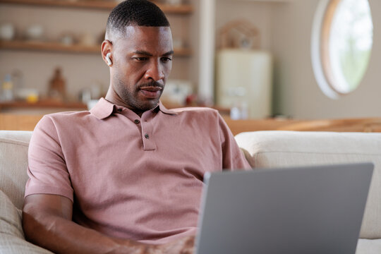 Man on couch with laptop and earbuds.