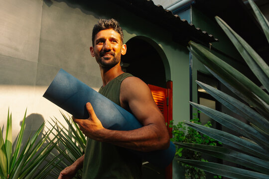 Man Carries Yoga Mat in Outdoor Space During Morning Light