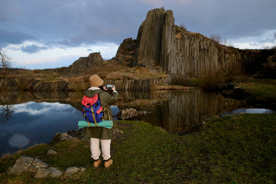 Traveler photographing basalt columns by reflective lake
