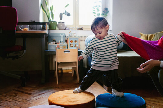 Toddler Balancing on Cushions While Holding Parent Hand