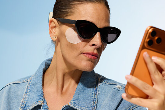 Woman Checking Phone While Wearing Sunglasses and Skincare Patch