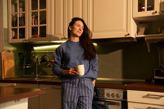 Woman standing by counter watching sunset outside