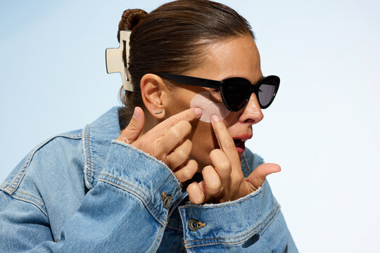 Woman Applying Skincare Product While Wearing Sunglasses Indoors