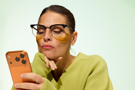 Woman With Glasses Checks Phone While Wearing Eye Patches