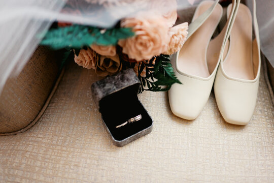 close up of ring in box and flat women's shoes and bouquet at wedding 