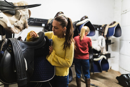 Two Women Organizing Equestrian Gear in a Stable Tack Room