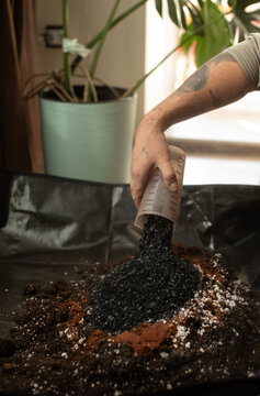 Anonymous man pouring coal into soil for house plants