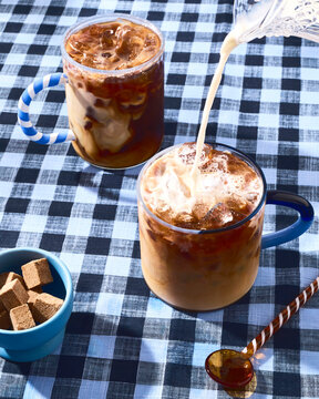 Iced coffee with milk pouring into glass mug