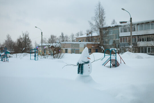 Snowman Stands in a Snowy Playground With Apartment Buildings Nearby
