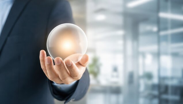 Crystal Ball of Insight: A businessman's outstretched hand holds a glowing crystal ball, symbolizing foresight and the intangible elements of business strategy in a modern office setting.