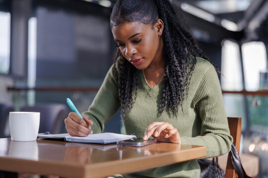 Woman taking notes while researching on smartphone