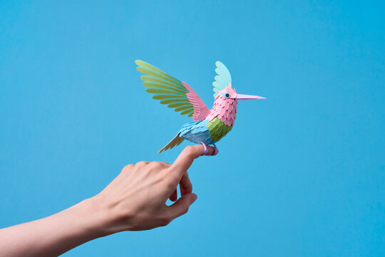 Paper hummingbird perched on finger, blue
