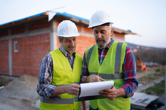 Two workers check plans on a construction site